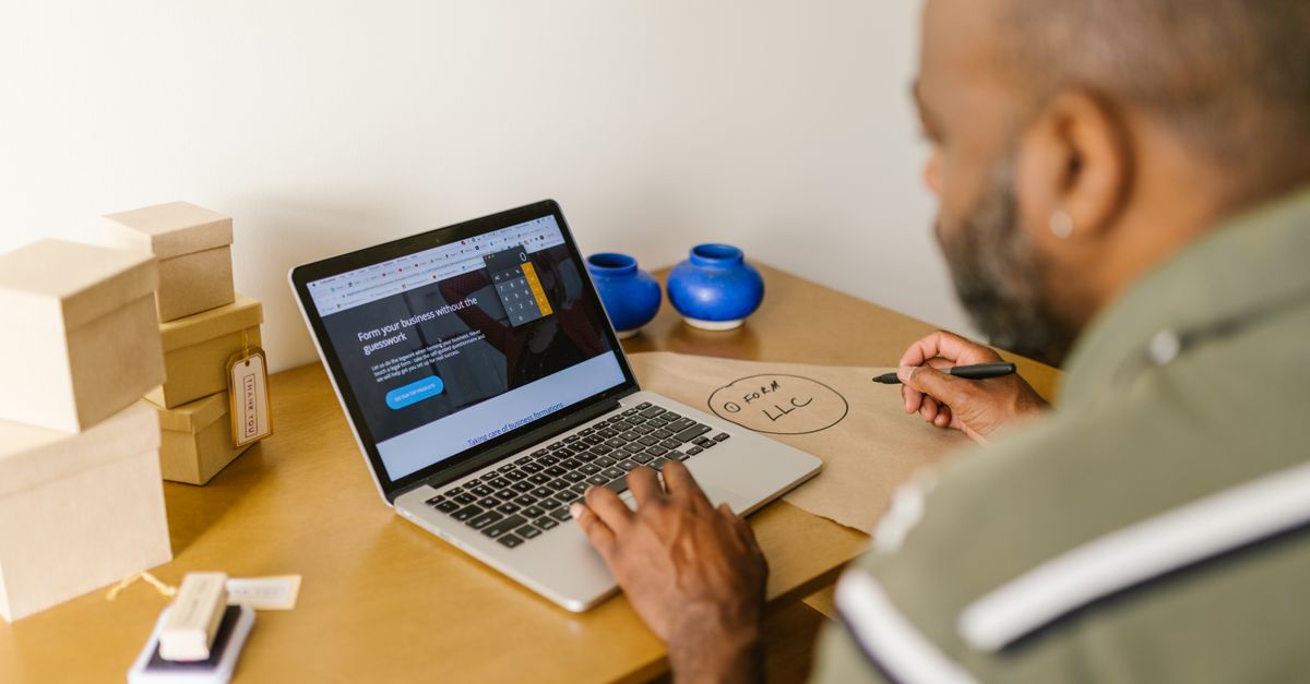 Pequeño emprendedor mirando un sitio web en la laptop, con cajas de productos sobre la mesa