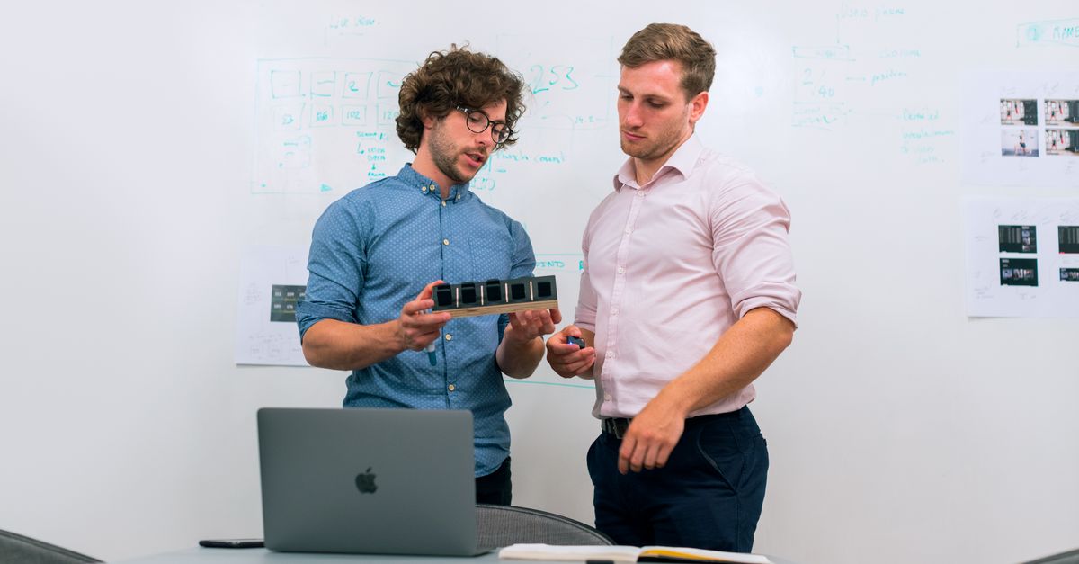 Dois fundadores de startup analisando um protótipo em frente ao quadro de planejamento